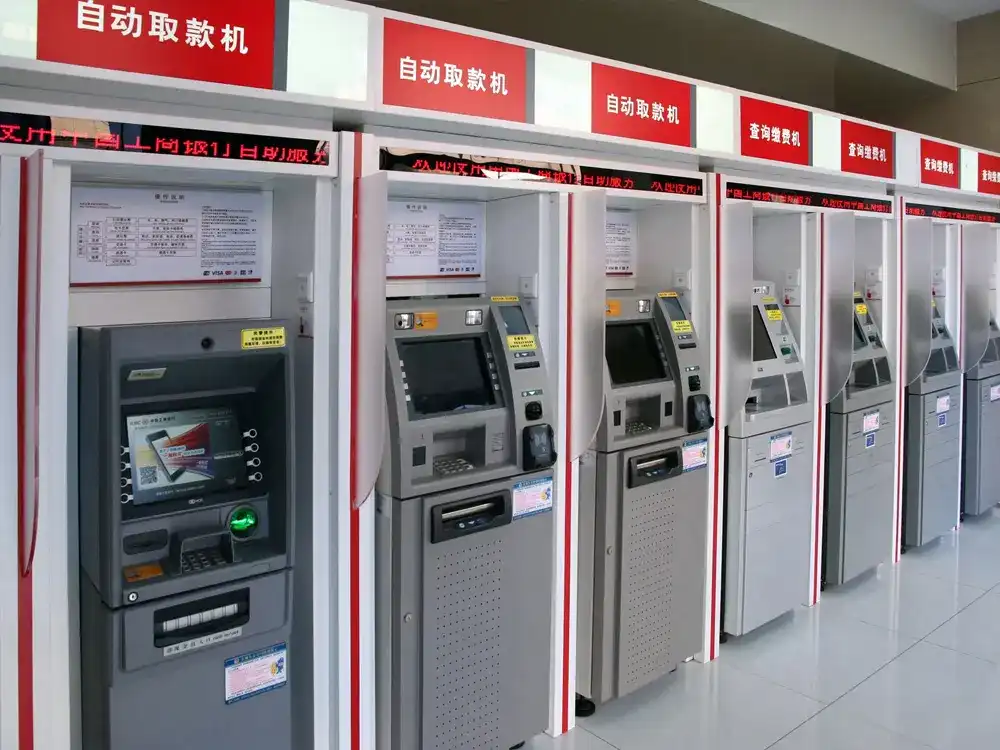 A row of modern self-service banking terminals and ATMs in a clean, indoor facility, featuring touchscreens and integrated signage for 24/7 financial services.