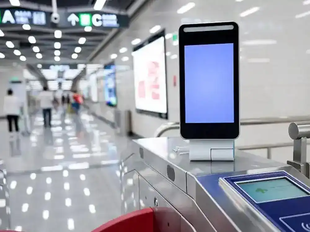 A high-tech security turnstile in a train station or airport equipped with a facial recognition tablet and RFID scanner for automated, contactless entry control.